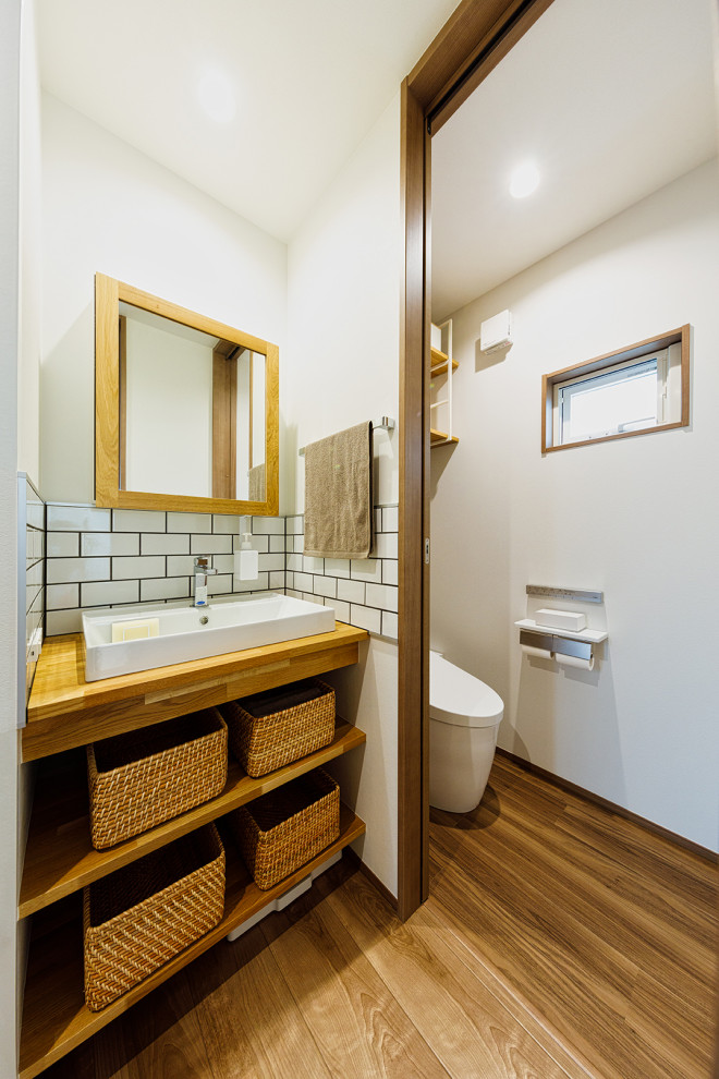 Medium sized contemporary cloakroom in Tokyo Suburbs with open cabinets, white cabinets, a one-piece toilet, white tiles, white walls, medium hardwood flooring, brown floors, white worktops, a wallpapered ceiling, wallpapered walls, ceramic tiles, a built-in sink, wooden worktops and a built in vanity unit.