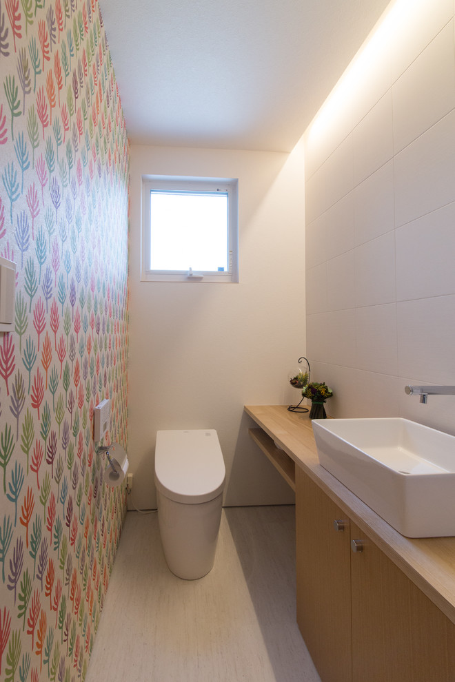 Photo of a small modern cloakroom with flat-panel cabinets, medium wood cabinets, multi-coloured walls, a vessel sink, wooden worktops and white floors.