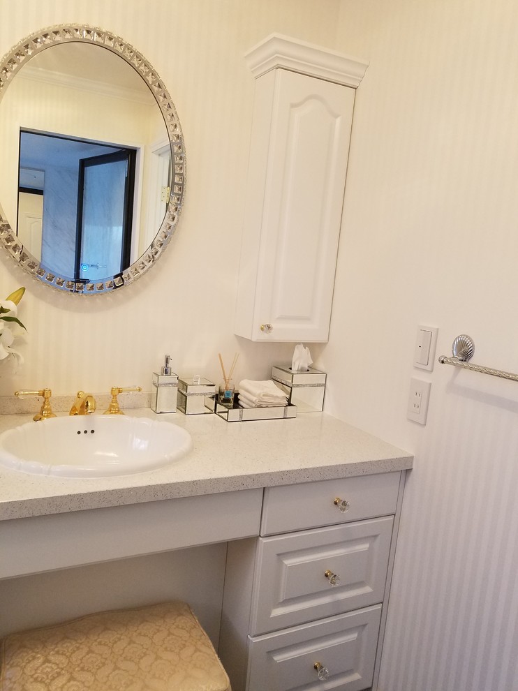 Foto på ett beige toalett, med möbel-liknande, vita skåp, vita väggar, ett nedsänkt handfat, bänkskiva i akrylsten och svart golv