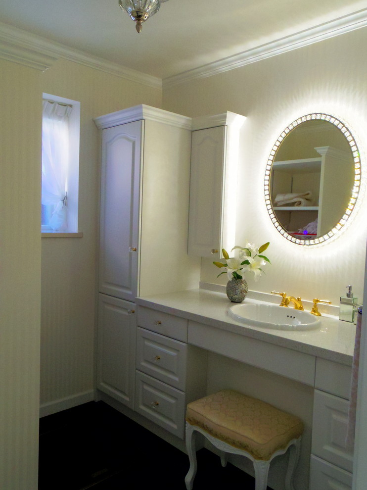 Cette photo montre un WC et toilettes avec un placard en trompe-l'oeil, des portes de placard blanches, un mur blanc, un lavabo posé, un plan de toilette en surface solide, un sol noir et un plan de toilette beige.