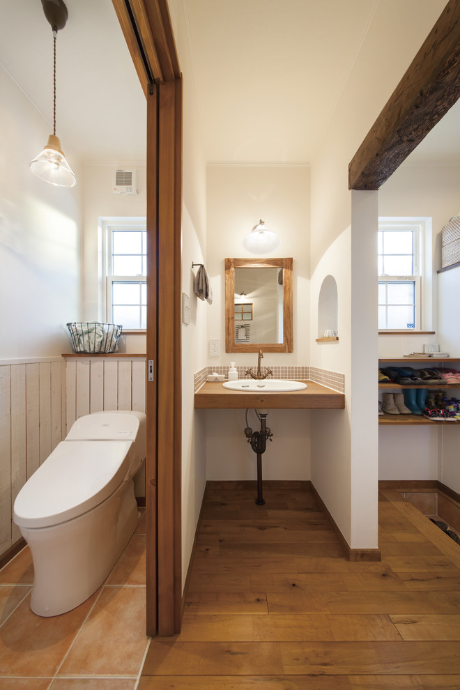 Bild på ett lantligt toalett, med vita väggar, mellanmörkt trägolv, ett nedsänkt handfat och brunt golv