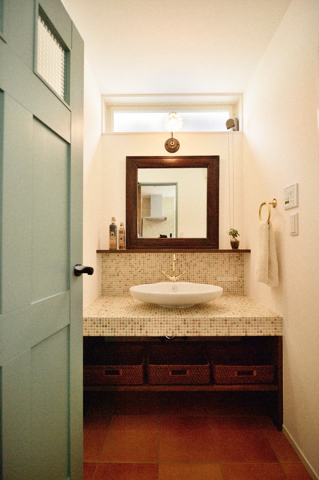 Exemple d'un WC et toilettes scandinave avec un placard sans porte, un mur blanc, tomettes au sol, une vasque, un plan de toilette en carrelage et un sol marron.