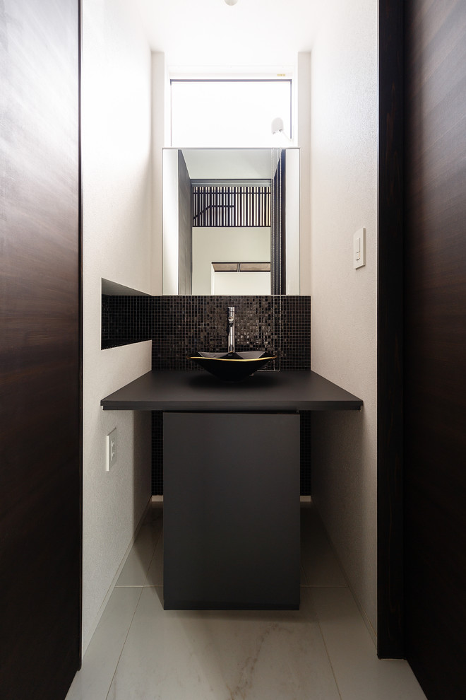 Foto di un ampio bagno di servizio moderno con ante nere, WC monopezzo, piastrelle nere, piastrelle a mosaico, pavimento con piastrelle in ceramica, pavimento bianco e top nero
