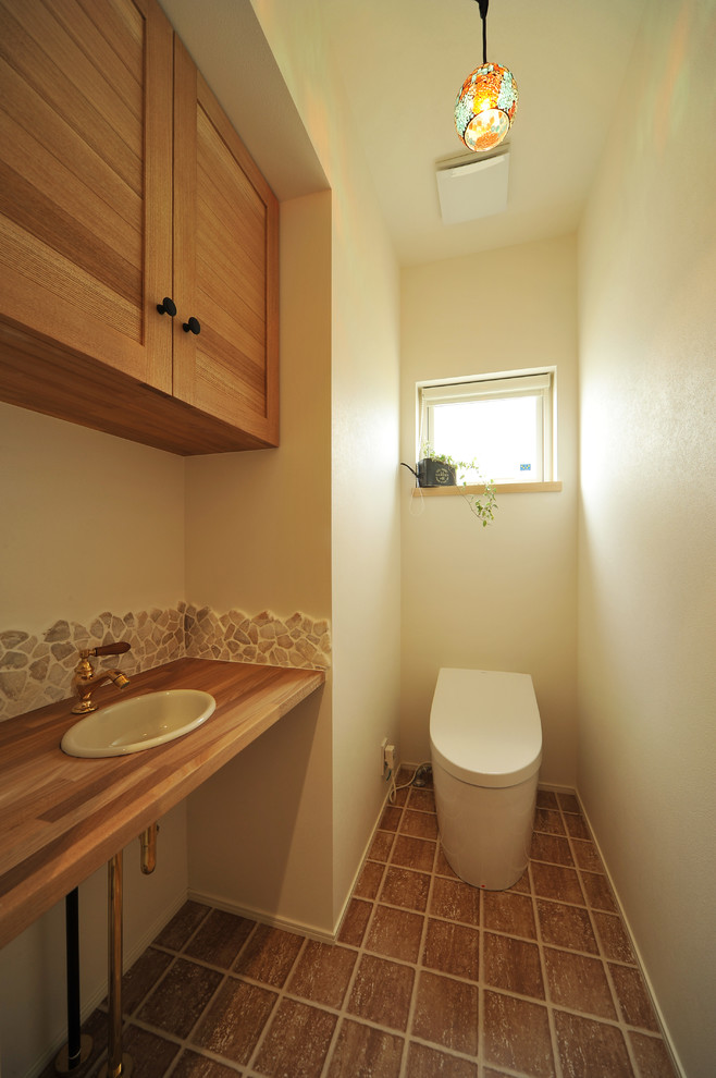 他の地域にあるアジアンスタイルのおしゃれなトイレ・洗面所 (落し込みパネル扉のキャビネット、中間色木目調キャビネット、白い壁、木製洗面台、茶色い床、ブラウンの洗面カウンター) の写真
