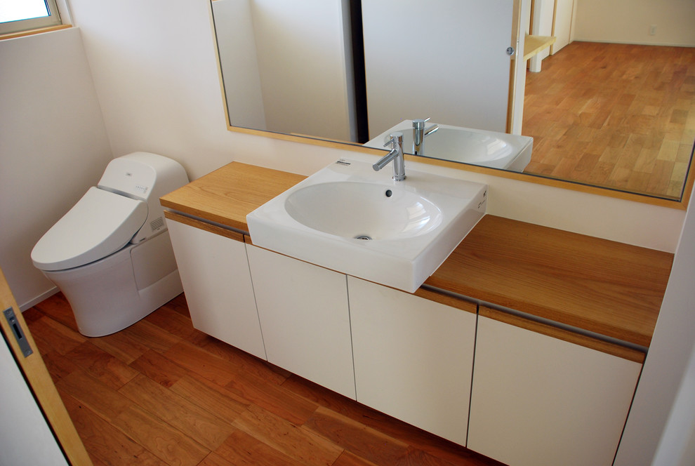 Exemple d'un petit WC et toilettes moderne avec un placard à porte plane, des portes de placard blanches, WC à poser, un carrelage blanc, un mur blanc, parquet foncé, une vasque, un plan de toilette en bois, un sol marron et un plan de toilette blanc.