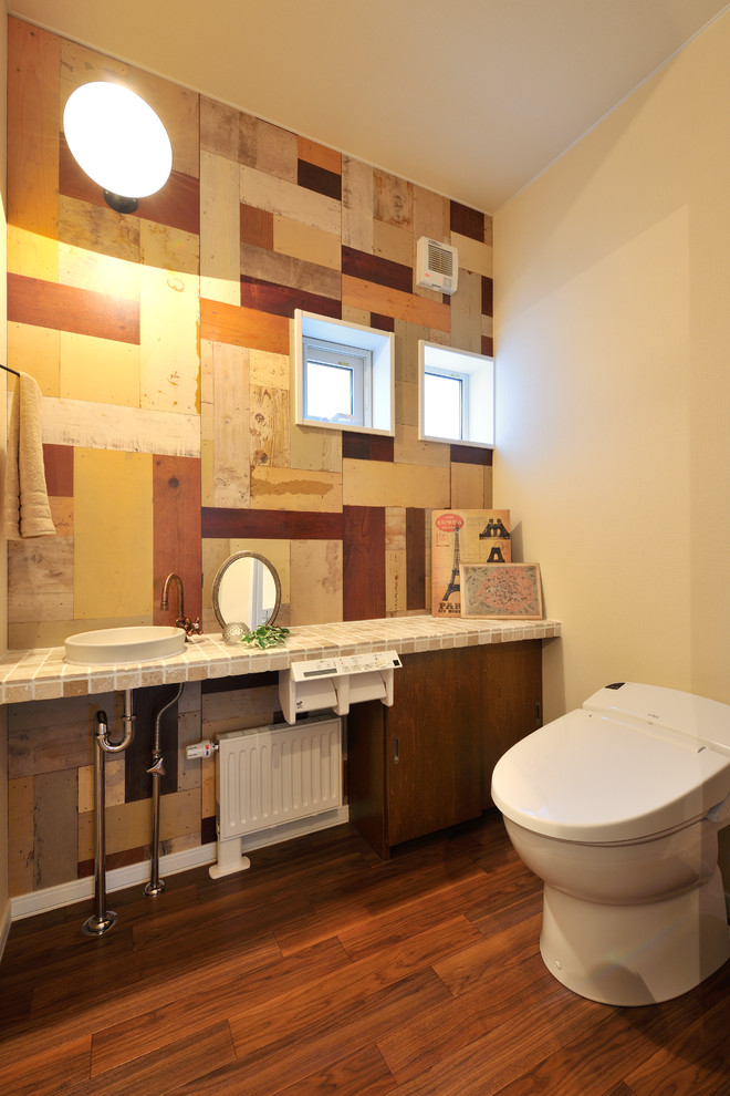 На фото: туалет в восточном стиле с плоскими фасадами, фасадами цвета дерева среднего тона, коричневой плиткой, бежевой плиткой, разноцветными стенами, паркетным полом среднего тона, накладной раковиной и коричневым полом с