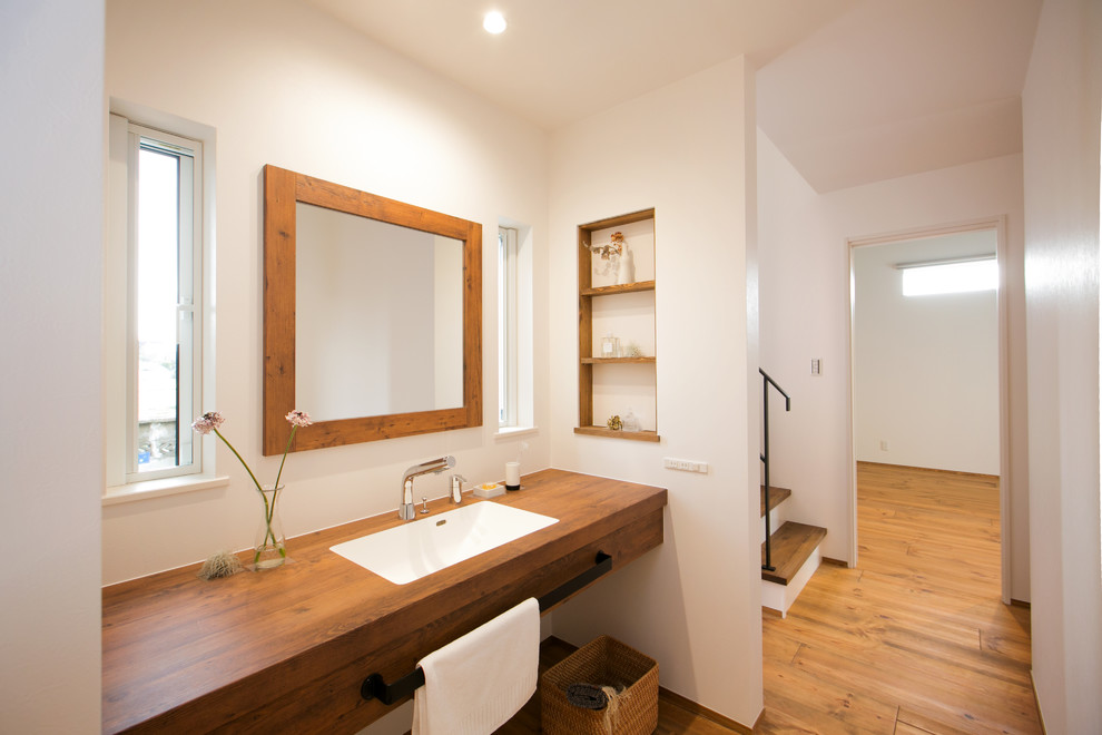 Asiatische Gästetoilette mit weißer Wandfarbe, braunem Holzboden, Waschtisch aus Holz, braunem Boden und brauner Waschtischplatte in Sonstige
