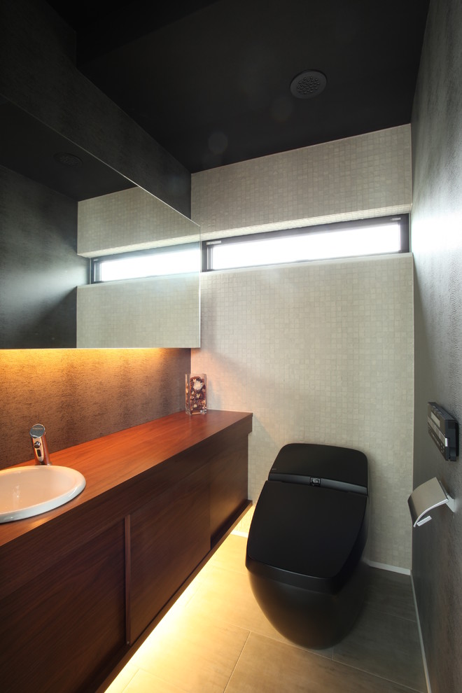 Foto på ett mellanstort funkis brun toalett, med släta luckor, skåp i mörkt trä, en toalettstol med hel cisternkåpa, beige kakel, travertin golv, ett nedsänkt handfat, träbänkskiva och grått golv