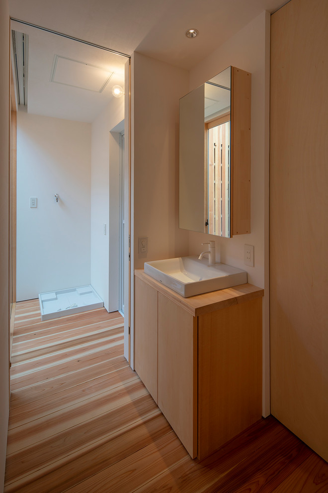 Kleine Asiatische Gästetoilette mit Kassettenfronten, beigen Schränken, Waschtisch aus Holz, weißer Waschtischplatte, weißer Wandfarbe, braunem Holzboden, Einbauwaschbecken und beigem Boden in Osaka