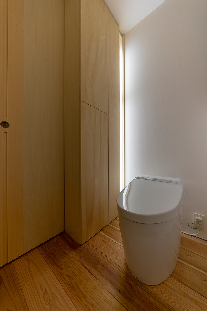 Modelo de aseo asiático con sanitario de una pieza, paredes blancas y suelo de madera en tonos medios