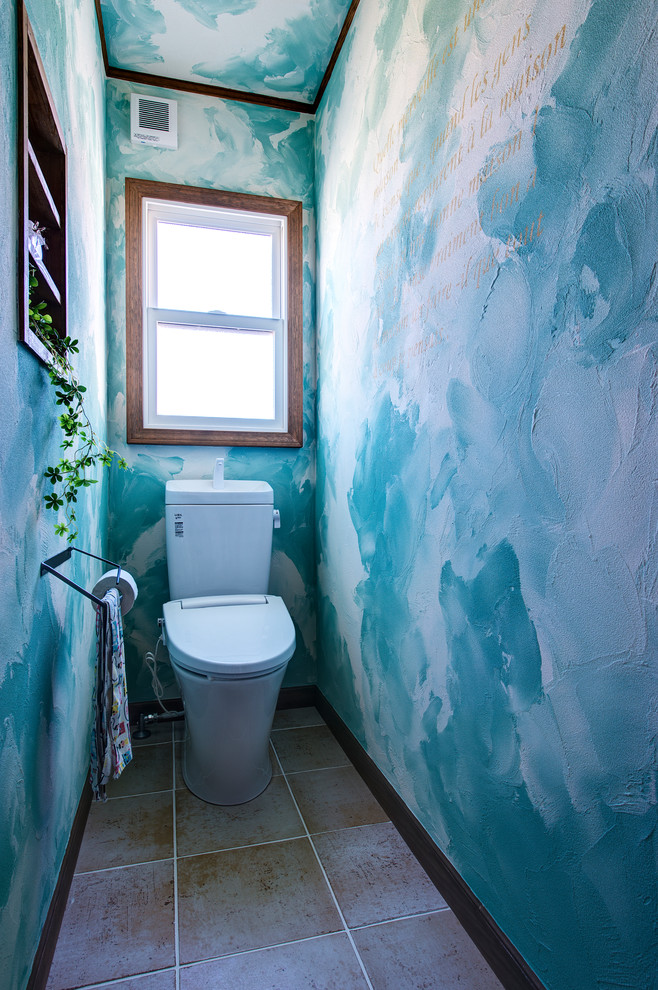 Cette image montre un WC et toilettes design avec un mur bleu, tomettes au sol et un sol marron.