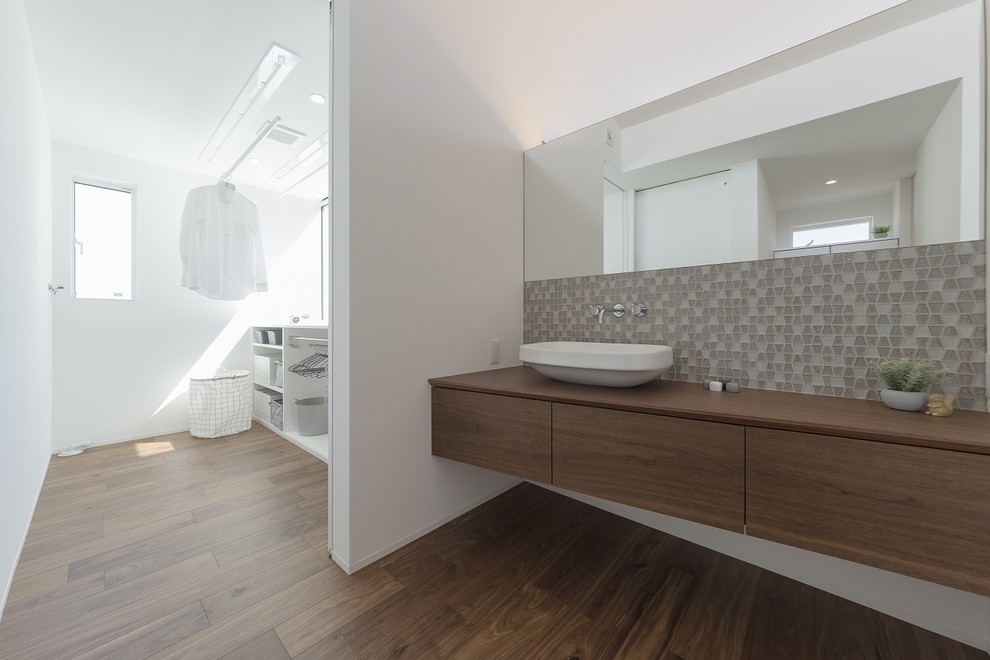 На фото: туалет в стиле модернизм с серой плиткой, белыми стенами, темным паркетным полом, настольной раковиной, столешницей из дерева, коричневым полом и коричневой столешницей