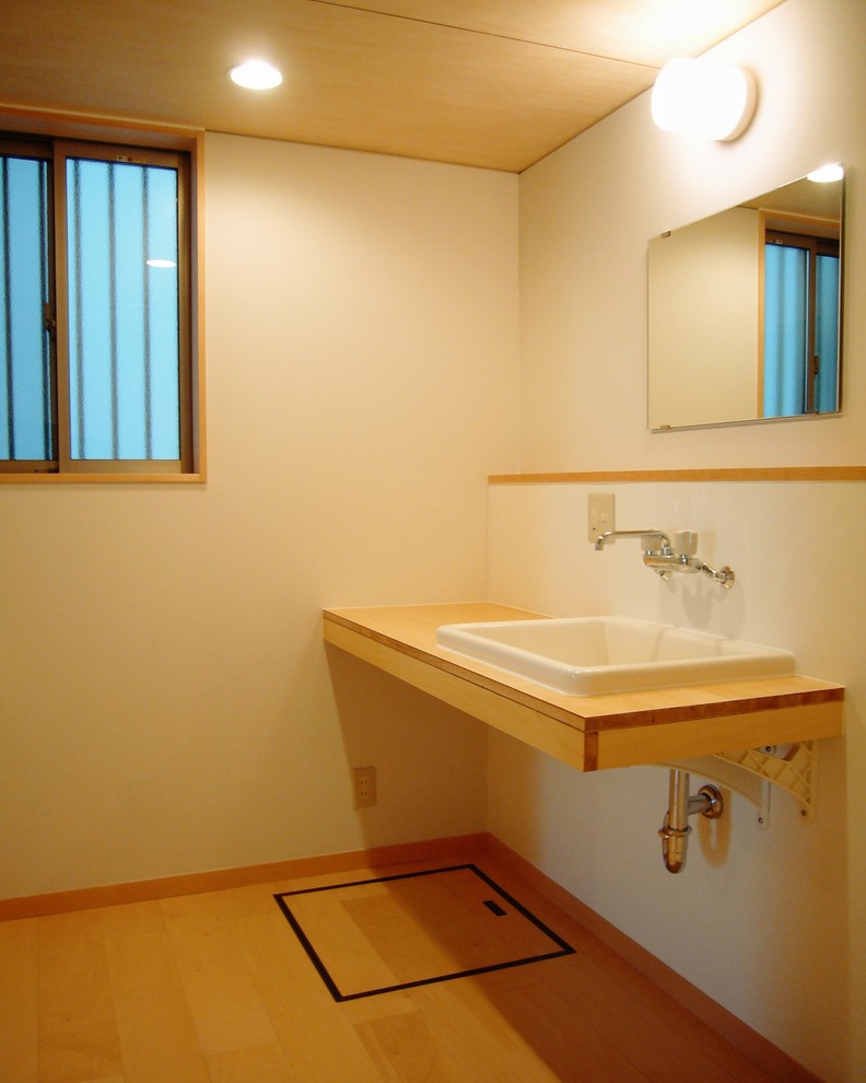 Cette image montre un petit WC et toilettes nordique en bois clair avec un mur blanc, un sol en contreplaqué, un lavabo posé, un plan de toilette en bois, un sol beige et un plan de toilette beige.