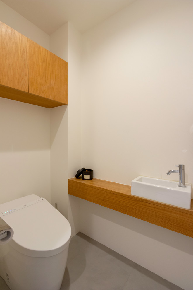 東京23区にあるコンテンポラリースタイルのおしゃれなトイレ・洗面所 (白い壁、木製洗面台、グレーの床、ブラウンの洗面カウンター) の写真