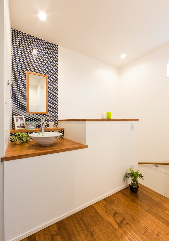Пример оригинального дизайна: туалет в современном стиле с синей плиткой, белыми стенами, паркетным полом среднего тона, столешницей из дерева и коричневым полом