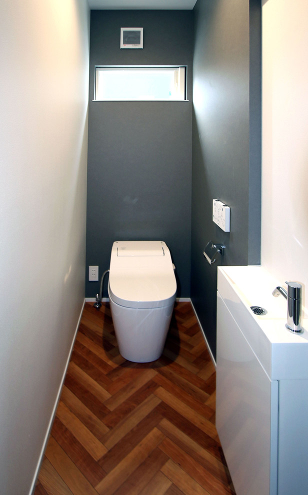 Powder room - modern laminate floor and brown floor powder room idea in Other with beaded inset cabinets, white cabinets, a one-piece toilet, blue walls, solid surface countertops and white countertops