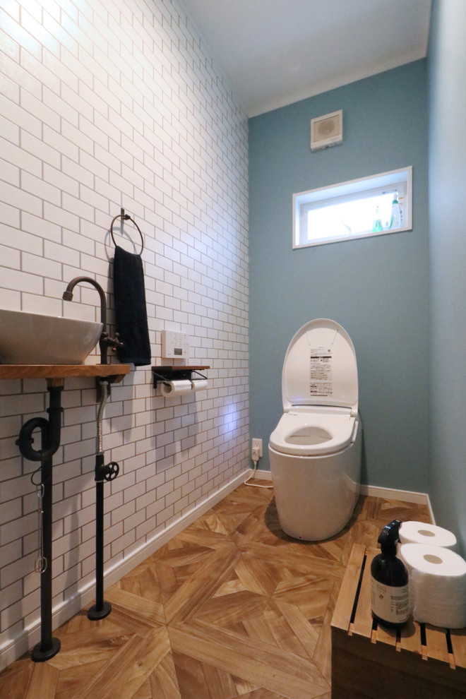 Idées déco pour un WC et toilettes campagne avec un carrelage blanc, un mur bleu, un sol en bois brun, une vasque, un plan de toilette en bois et un sol marron.