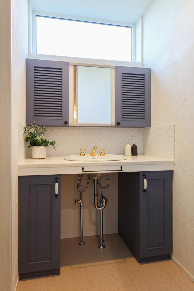 他の地域にあるミッドセンチュリースタイルのおしゃれなトイレ・洗面所 (落し込みパネル扉のキャビネット、青いキャビネット、白い壁、ベッセル式洗面器、ベージュの床) の写真