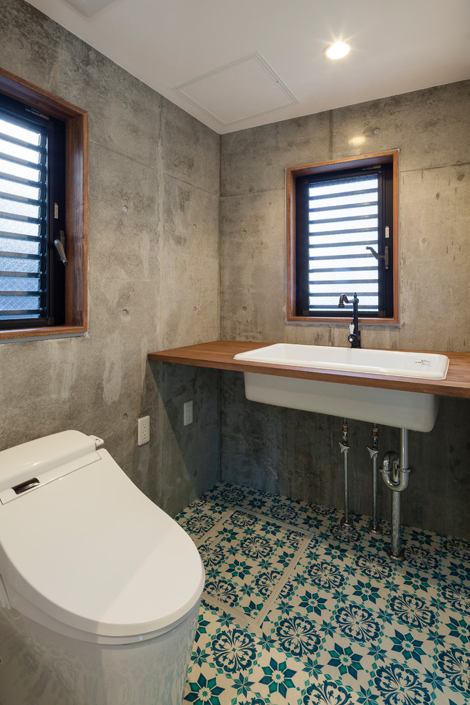 Bild på ett mellanstort industriellt vit vitt toalett, med en toalettstol med hel cisternkåpa, grå väggar, klinkergolv i porslin, ett nedsänkt handfat, träbänkskiva och blått golv