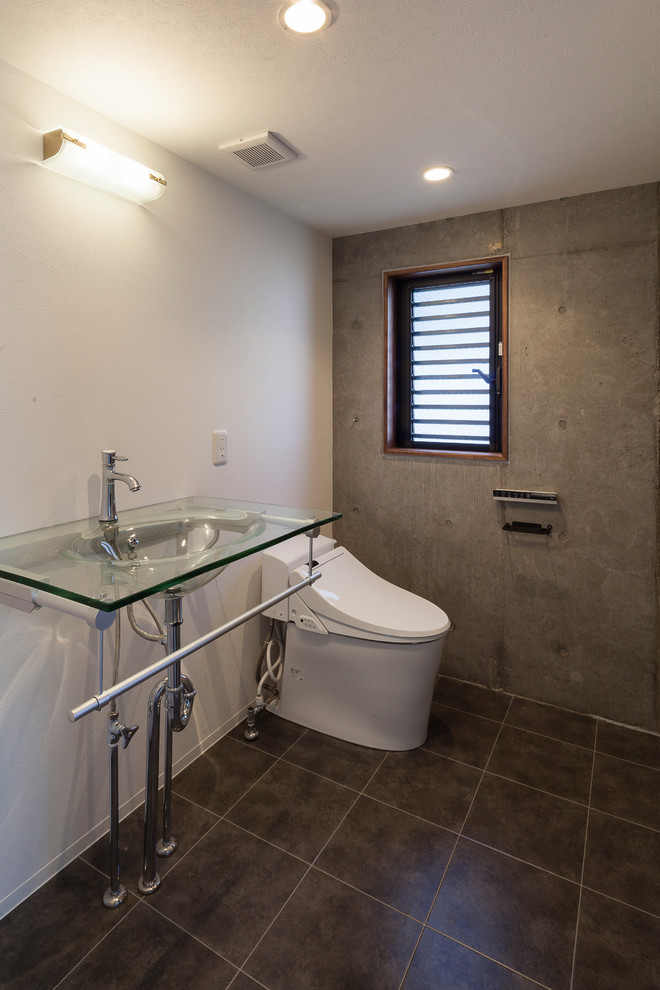 На фото: туалет среднего размера в стиле модернизм с унитазом-моноблоком, разноцветными стенами, полом из керамогранита, монолитной раковиной, стеклянной столешницей и серым полом