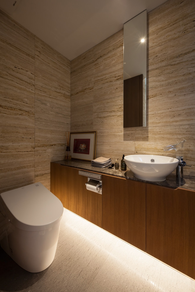 Inredning av ett asiatiskt brun brunt toalett, med släta luckor, skåp i mellenmörkt trä, bruna väggar, ett fristående handfat, marmorbänkskiva och vitt golv