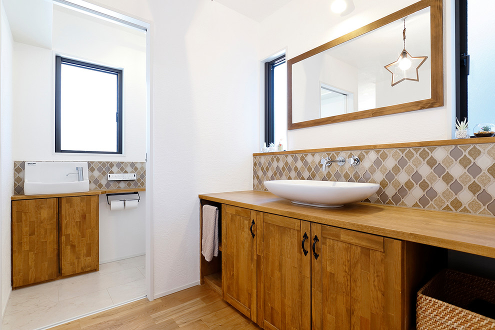 Foto på ett lantligt toalett, med släta luckor, skåp i slitet trä, vita väggar, mellanmörkt trägolv, ett fristående handfat och brunt golv