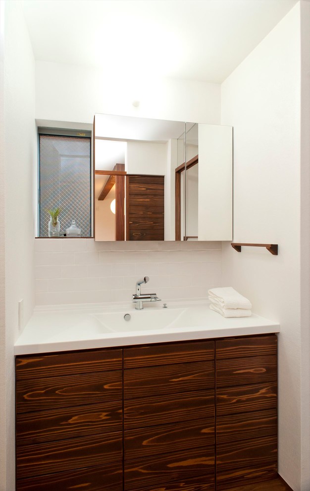 Asiatische Gästetoilette mit schwarz-weißen Fliesen, weißer Wandfarbe, dunklem Holzboden, integriertem Waschbecken, braunem Boden und weißer Waschtischplatte in Sonstige
