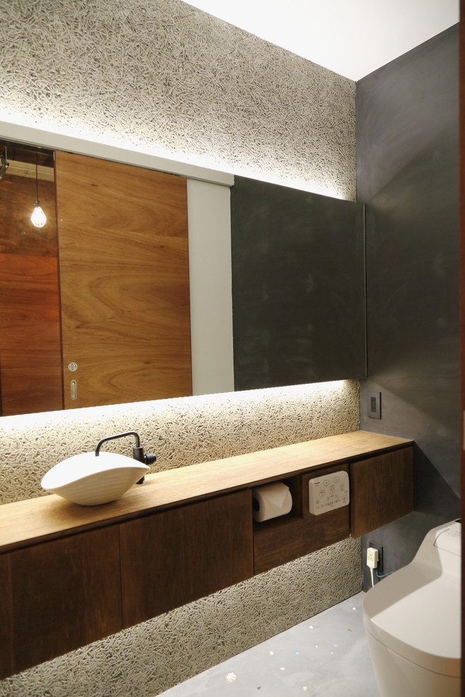 Asiatisk inredning av ett toalett, med släta luckor, skåp i slitet trä, grå väggar, ett fristående handfat och vitt golv
