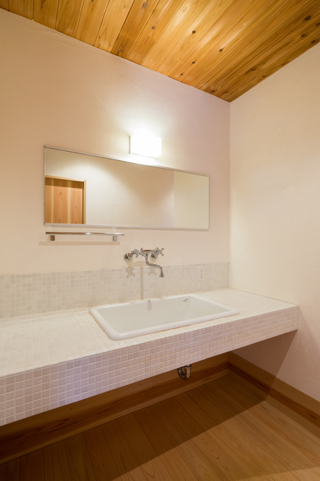 Cette photo montre un petit WC et toilettes moderne avec des portes de placard blanches, un carrelage blanc, des carreaux de porcelaine, un sol en bois brun, un plan de toilette blanc, meuble-lavabo encastré et un plafond en bois.