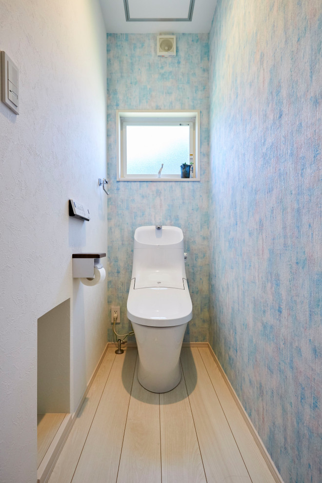 Modelo de aseo pequeño con sanitario de una pieza, baldosas y/o azulejos blancos, paredes azules, suelo de madera clara, suelo beige y papel pintado