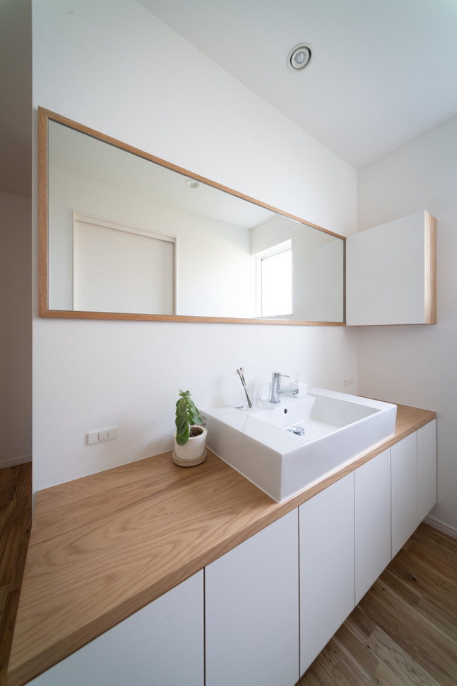 Design ideas for a world-inspired cloakroom in Other with white cabinets, white walls, light hardwood flooring, a console sink, flat-panel cabinets, wooden worktops, brown floors and beige worktops.