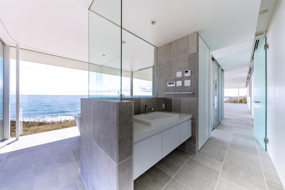 Пример оригинального дизайна: большой туалет в стиле модернизм с полом из керамогранита, серым полом, плоскими фасадами, белыми фасадами, белыми стенами и накладной раковиной
