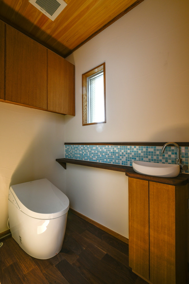 Idéer för ett stort asiatiskt brun toalett, med släta luckor, skåp i mellenmörkt trä, vita väggar, mörkt trägolv, ett fristående handfat och brunt golv