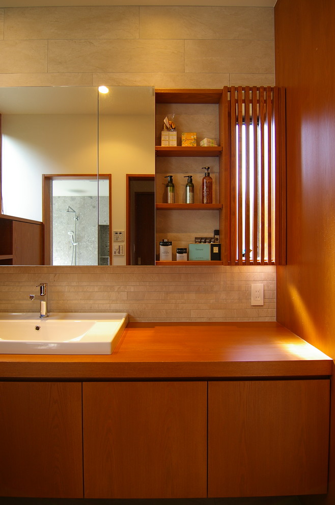Idée de décoration pour un WC et toilettes vintage en bois brun avec un placard sans porte, un carrelage gris, des carreaux de porcelaine, un mur blanc, une grande vasque, un plan de toilette en bois et un plan de toilette beige.