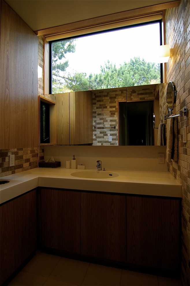 Aménagement d'un WC et toilettes rétro avec des portes de placard marrons, un carrelage beige, du carrelage en travertin, un mur beige, un lavabo intégré, un plan de toilette en surface solide, un plan de toilette blanc, un sol en vinyl et un sol marron.