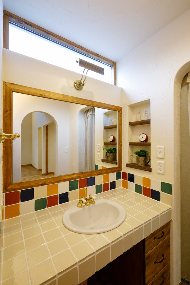 Cette image montre un WC et toilettes rustique en bois brun avec un placard à porte plane, un mur blanc, un lavabo posé, un plan de toilette en carrelage, un sol marron et un plan de toilette beige.