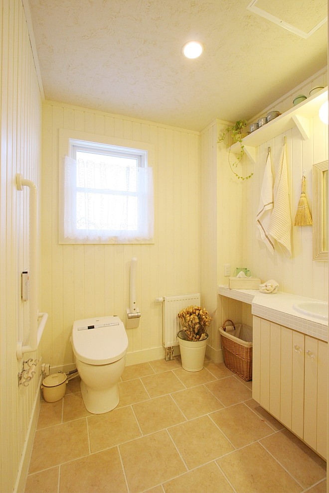他の地域にある広いシャビーシック調のおしゃれなトイレ・洗面所 (ベージュのキャビネット、ベージュの壁、テラコッタタイルの床、タイルの洗面台、ベージュの床、白い洗面カウンター) の写真