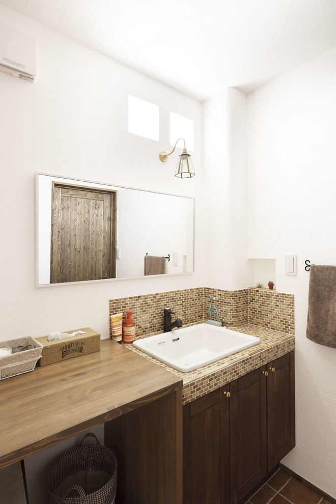Exemple d'un WC et toilettes nature en bois foncé avec un placard avec porte à panneau encastré, un carrelage marron, mosaïque, un mur blanc, tomettes au sol, un lavabo posé, un plan de toilette en carrelage, un sol orange et un plan de toilette marron.