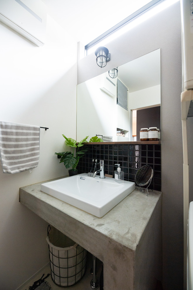 他の地域にあるインダストリアルスタイルのおしゃれなトイレ・洗面所 (黒いタイル、磁器タイル、白い壁、ベッセル式洗面器、コンクリートの洗面台、グレーの洗面カウンター) の写真