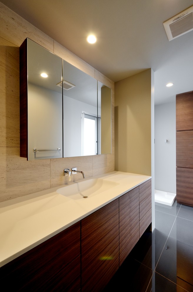 Cette image montre un WC et toilettes minimaliste en bois foncé avec un carrelage beige, du carrelage en pierre calcaire, un mur beige, un sol en carrelage de porcelaine, un lavabo intégré, un plan de toilette en surface solide et un sol noir.