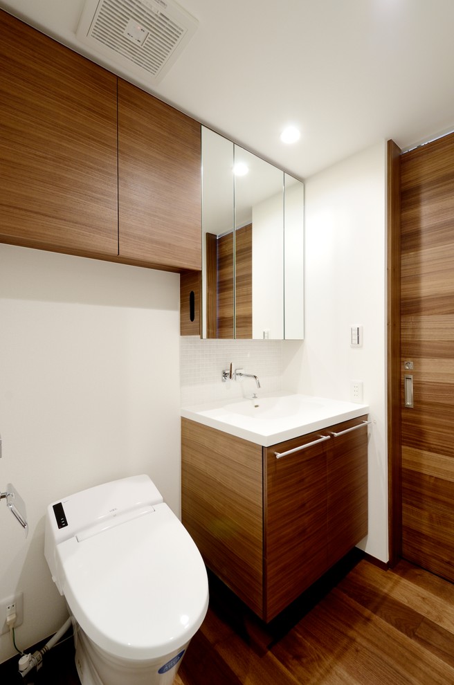 This is an example of a modern cloakroom in Tokyo Suburbs with brown cabinets, a one-piece toilet, white tiles, glass tiles, white walls, dark hardwood flooring, an integrated sink, solid surface worktops and brown floors.