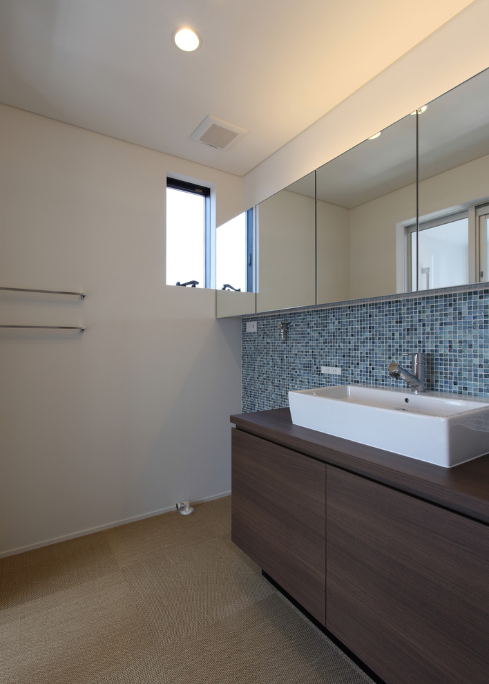 Idée de décoration pour un WC et toilettes minimaliste en bois foncé avec un placard à porte plane, un carrelage bleu, mosaïque, un mur blanc, une vasque, un plan de toilette en bois et un sol beige.