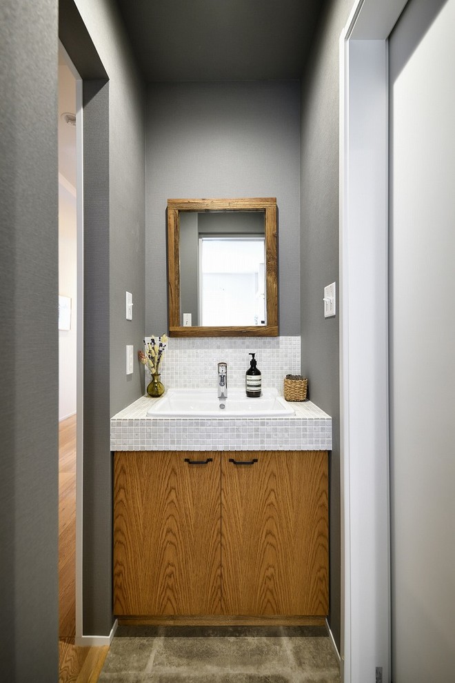 トランジショナルスタイルのおしゃれなトイレ・洗面所 (フラットパネル扉のキャビネット、中間色木目調キャビネット、グレーの壁、オーバーカウンターシンク、茶色い床、白い洗面カウンター) の写真