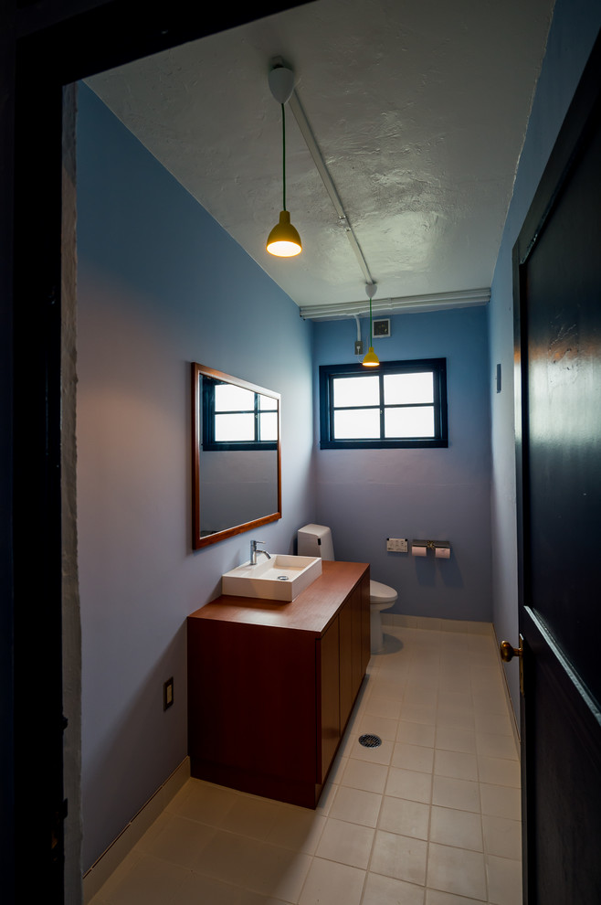 Aménagement d'un WC et toilettes rétro en bois brun avec un placard à porte plane, WC à poser, une vasque, un plan de toilette en bois, un sol beige, un mur bleu, un plan de toilette marron, un sol en carrelage de porcelaine et meuble-lavabo encastré.