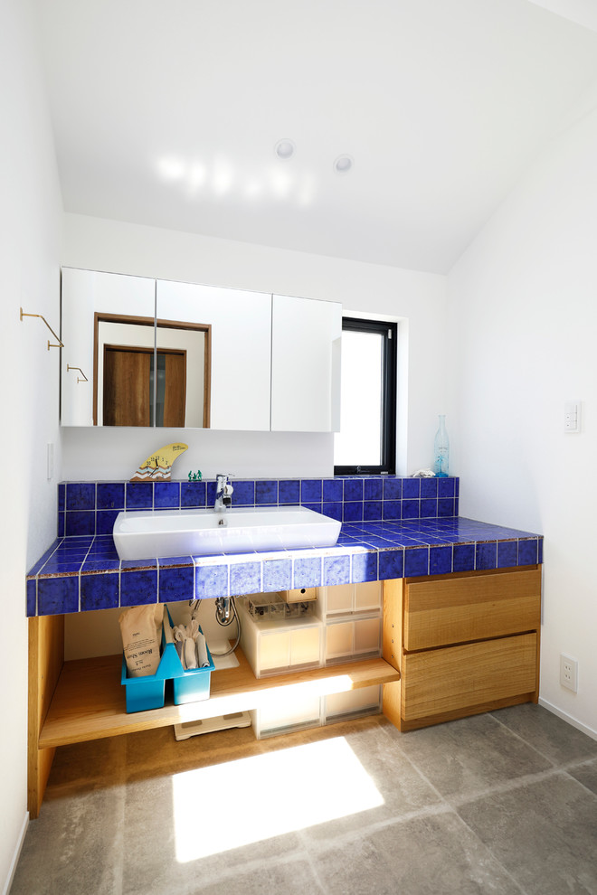 ビーチスタイルのおしゃれなトイレ・洗面所 (フラットパネル扉のキャビネット、中間色木目調キャビネット、白い壁、コンクリートの床、ベッセル式洗面器、グレーの床) の写真