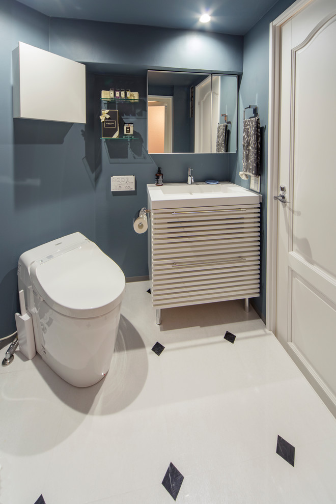 На фото: туалет в морском стиле с фасадами с филенкой типа жалюзи, белыми фасадами, синими стенами, полом из керамической плитки, монолитной раковиной и разноцветным полом с