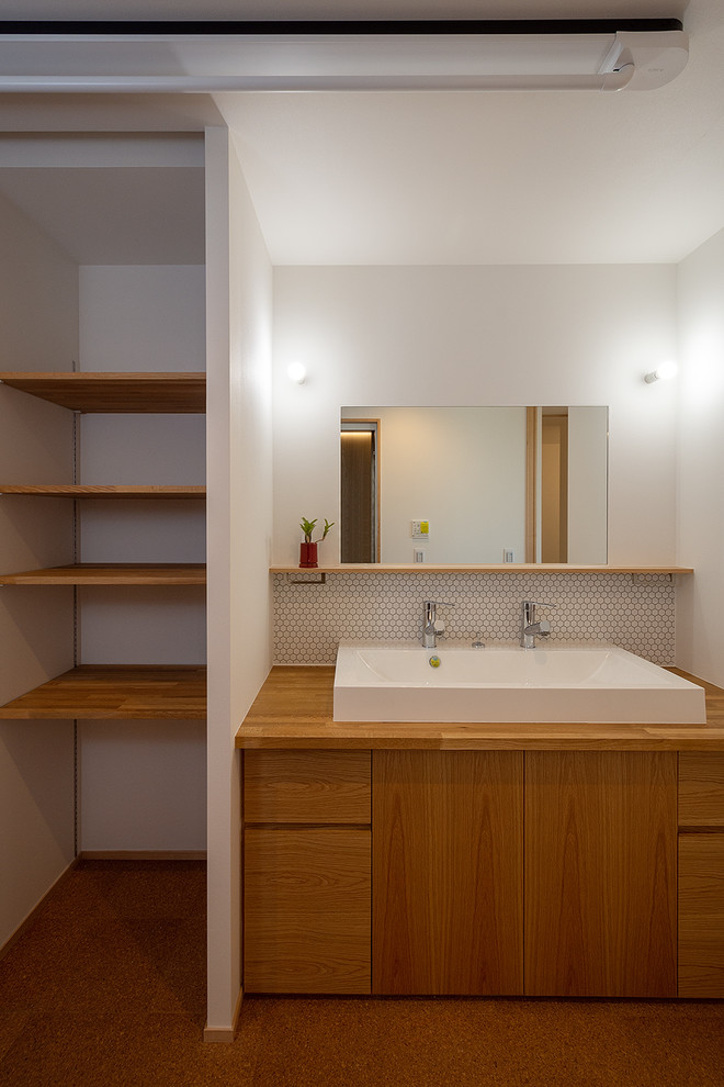 Inspiration för mellanstora minimalistiska brunt toaletter, med släta luckor, skåp i mellenmörkt trä, vita väggar, ett fristående handfat, träbänkskiva, vit kakel, mosaik, korkgolv och brunt golv