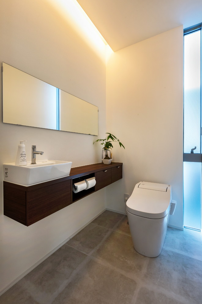 Стильный дизайн: туалет в современном стиле с белыми стенами, бетонным полом, серым полом, плоскими фасадами, темными деревянными фасадами, инсталляцией, настольной раковиной и столешницей из дерева - последний тренд
