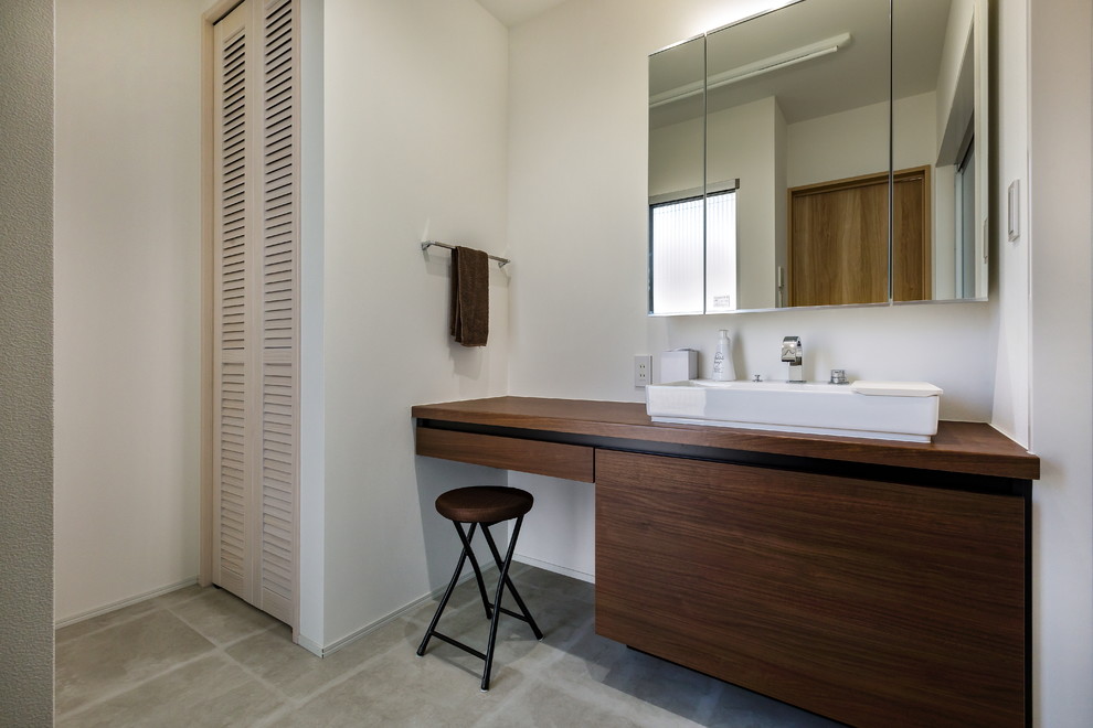 Пример оригинального дизайна: туалет в современном стиле с плоскими фасадами, белыми стенами, бетонным полом, настольной раковиной, столешницей из дерева, серым полом и темными деревянными фасадами