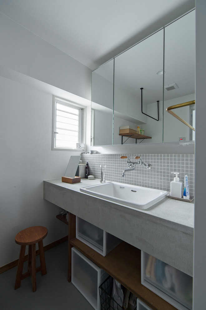 Foto på ett litet funkis grå toalett, med öppna hyllor, grå kakel, mosaik, vita väggar, skåp i mellenmörkt trä, betonggolv, ett nedsänkt handfat, bänkskiva i betong och grått golv